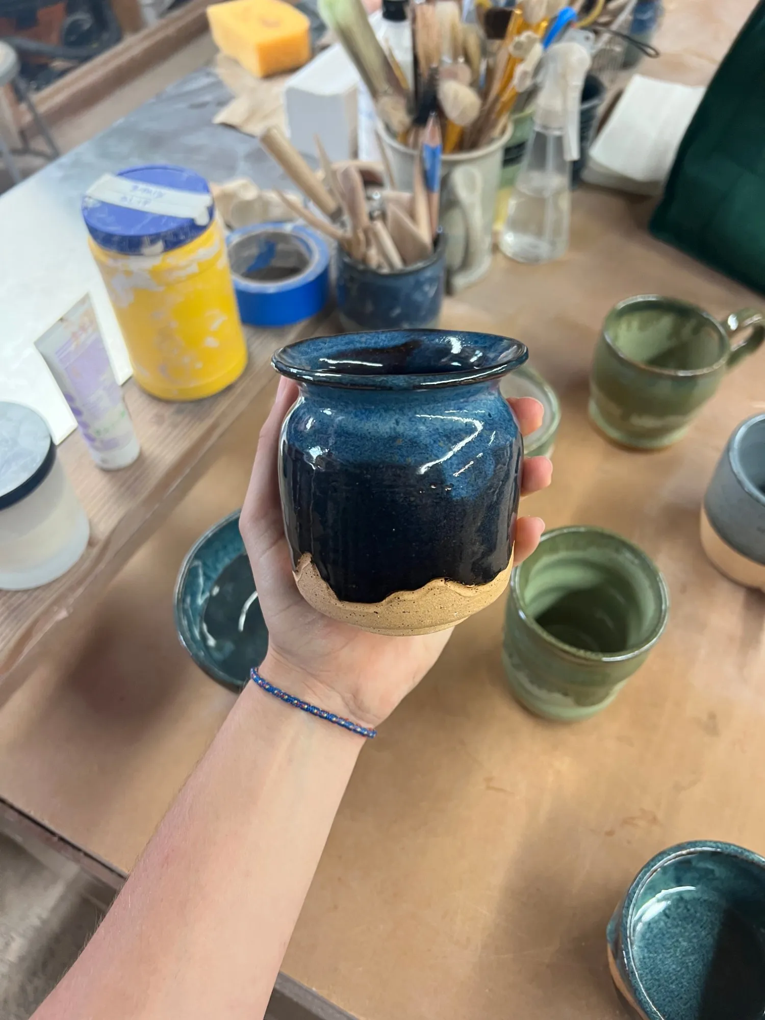 A small jar glazed deep blue with a bare clay foot, held in a hand