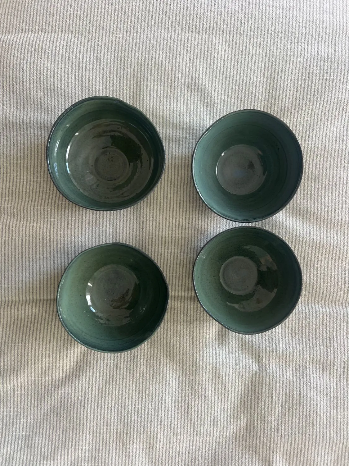Four green glazed bowls seen from above on a striped cloth
