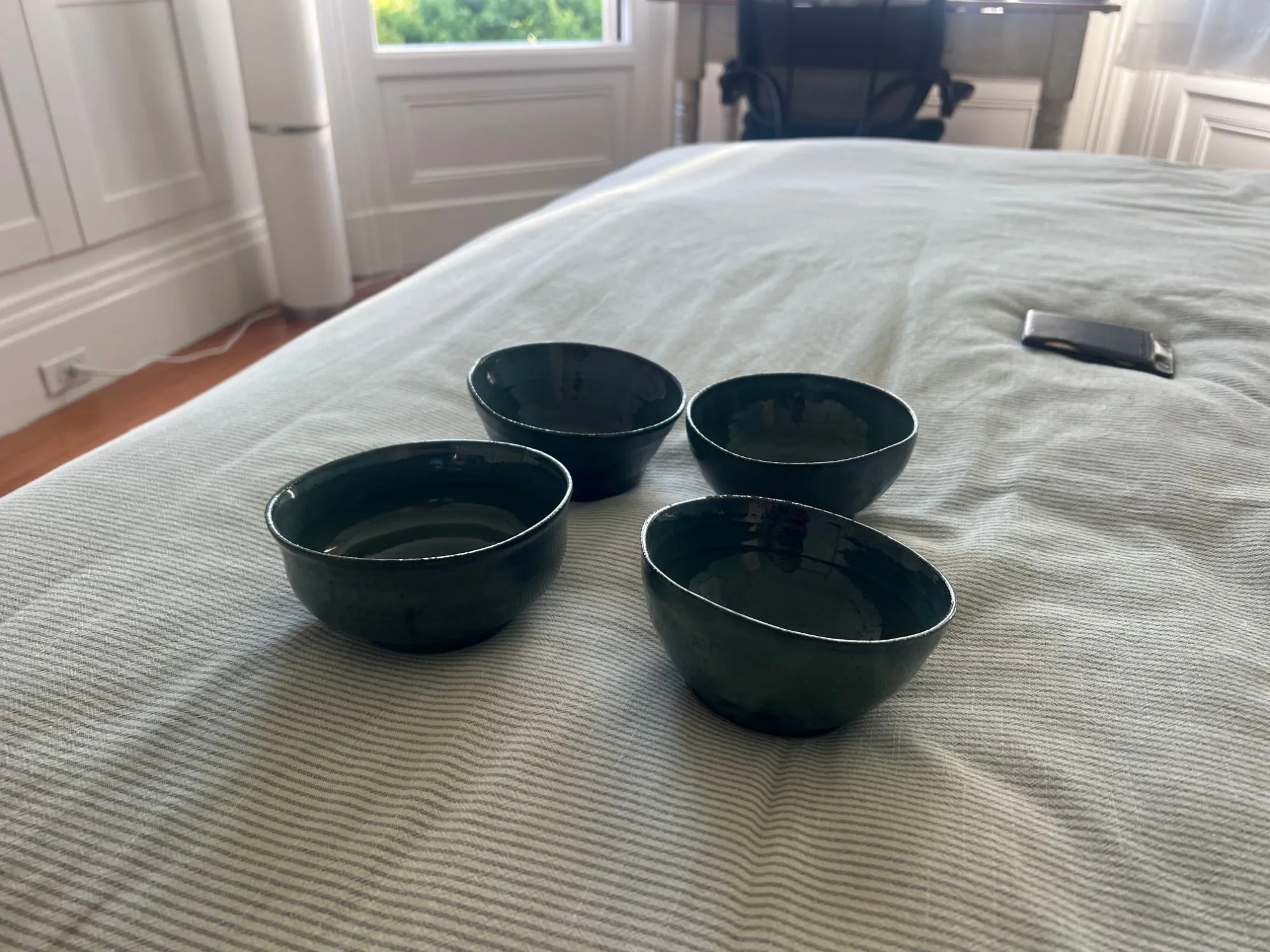 Four dark green glazed bowls on a bed