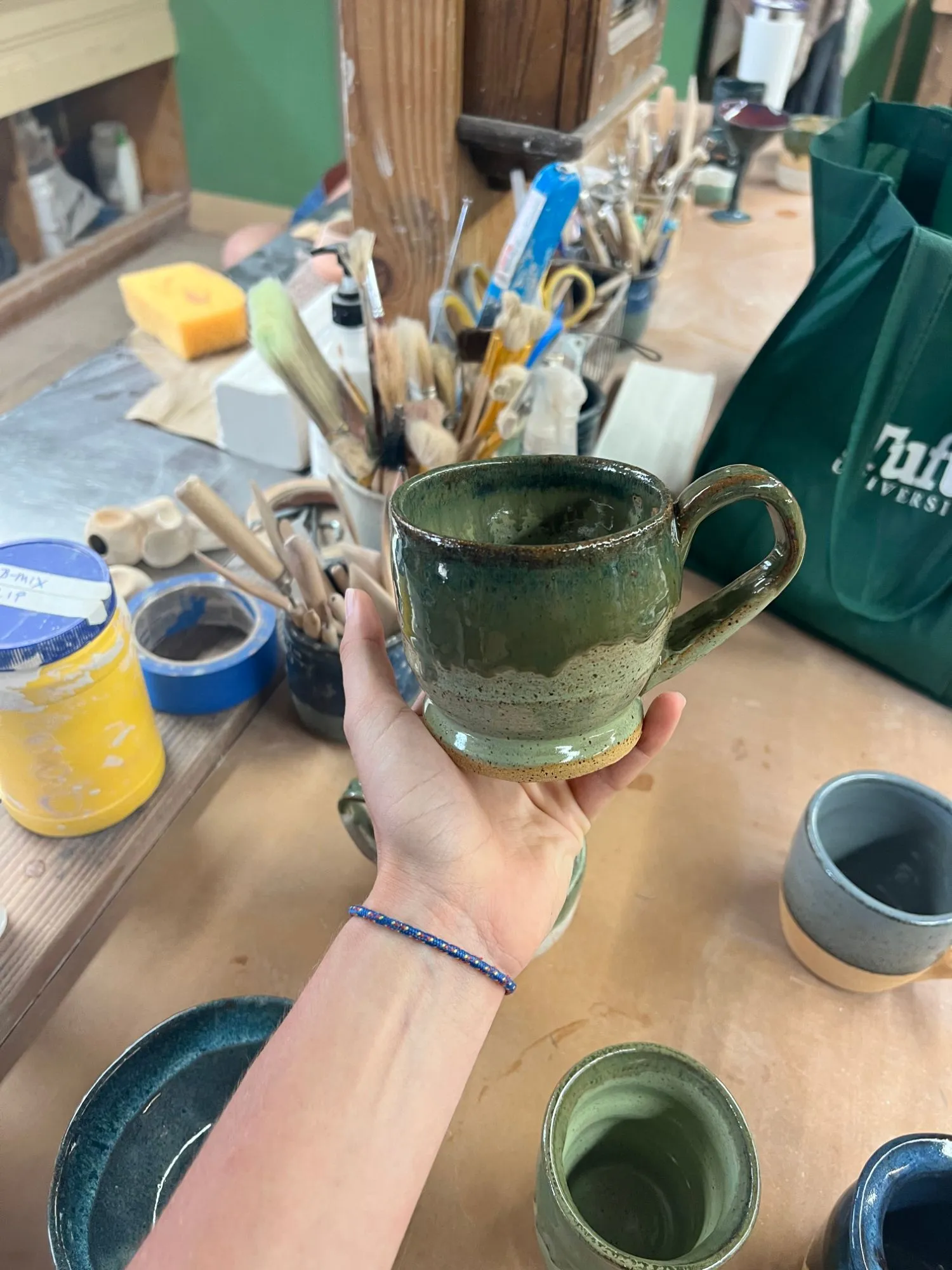 A green speckled mug with a handle, held in a hand