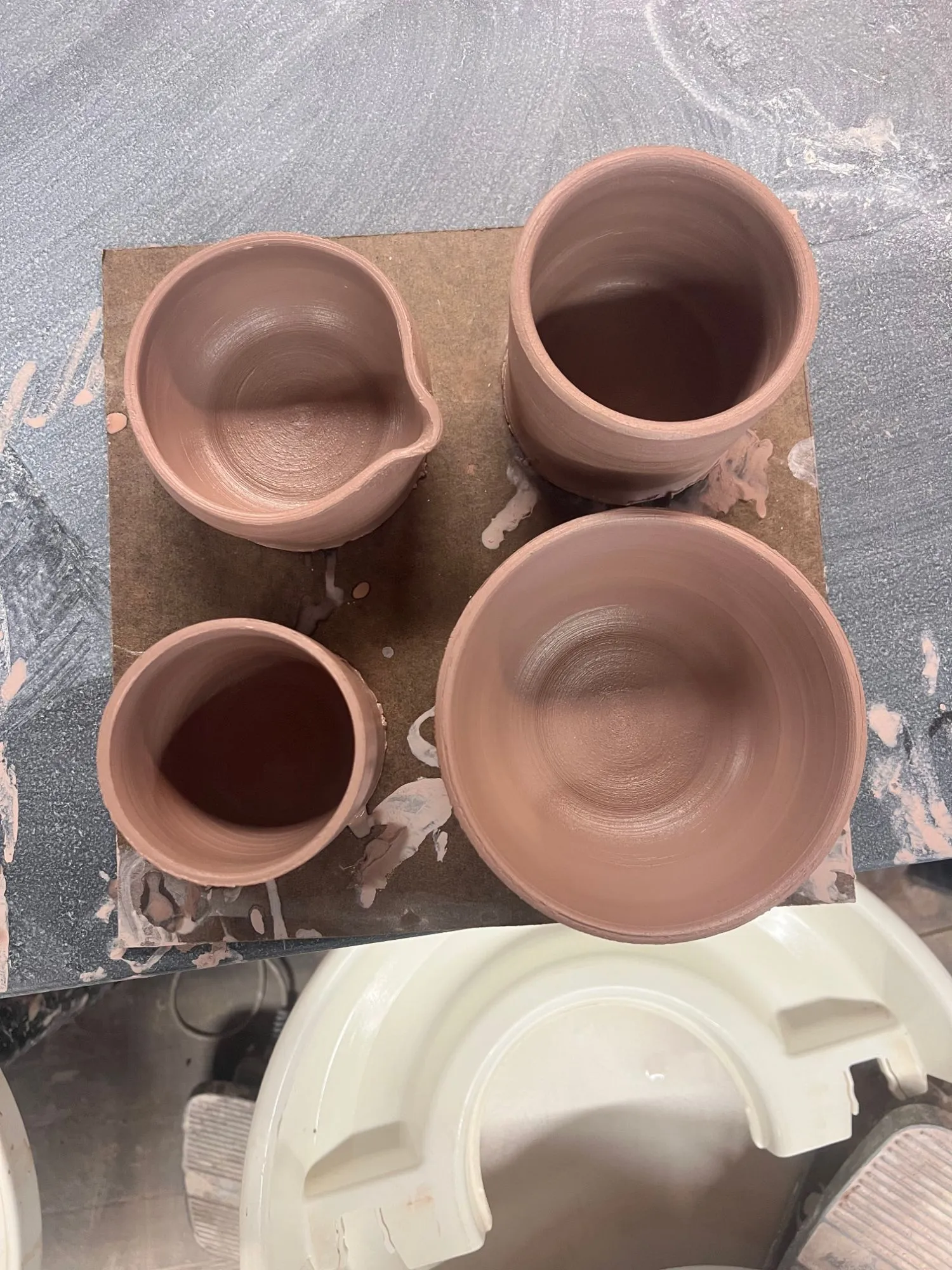 A pitcher, two cups, and a bowl in unfired clay, seen from above
