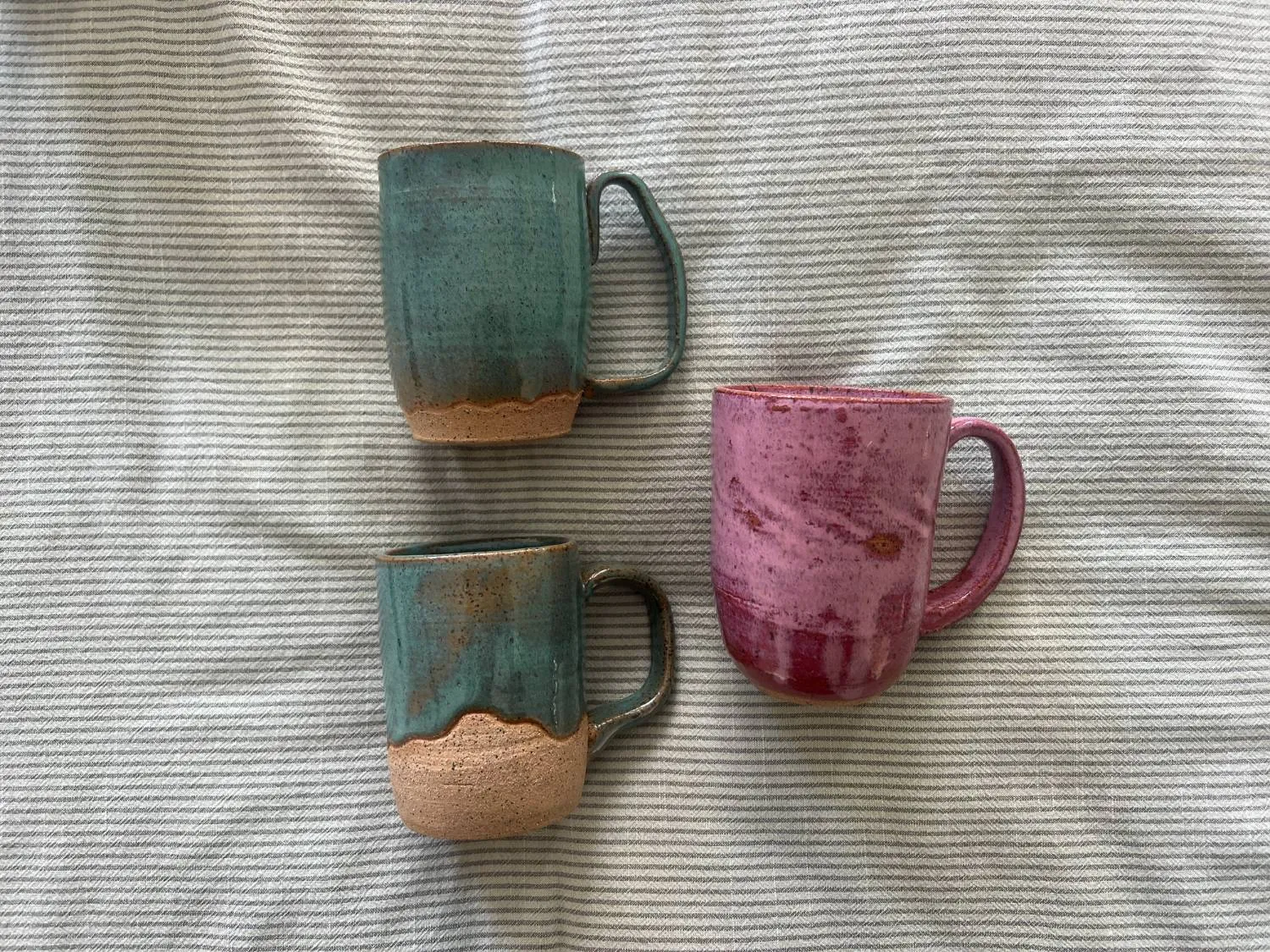 Two teal mugs and a pink mug lying on a striped cloth