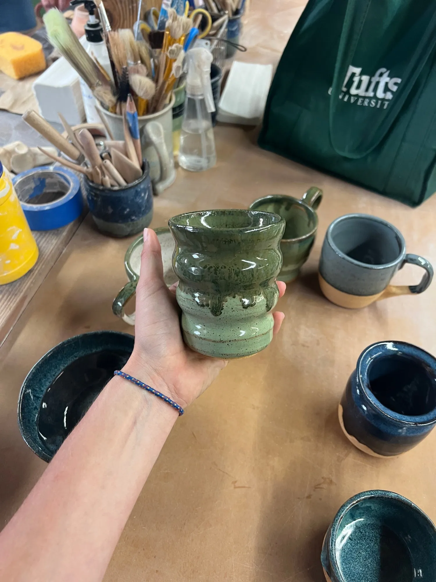A wavy cup glazed green with dark drips, held in a hand