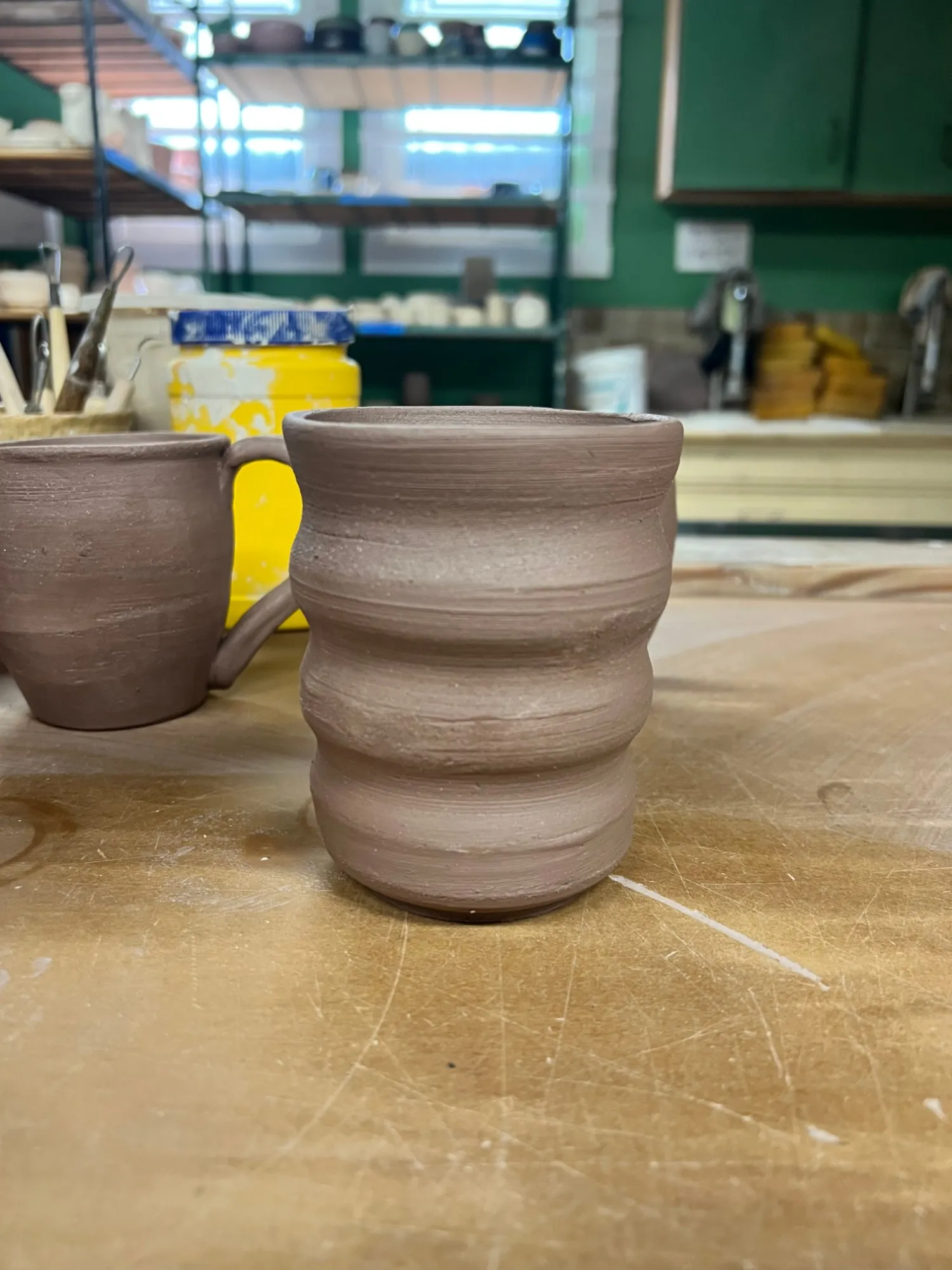 A wavy, unglazed clay cup on a studio table
